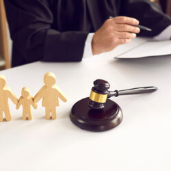 Silhouettes en bois d'une famille posées sur un bureau, avec à côté un marteau de justice et des mains tenant un dossier