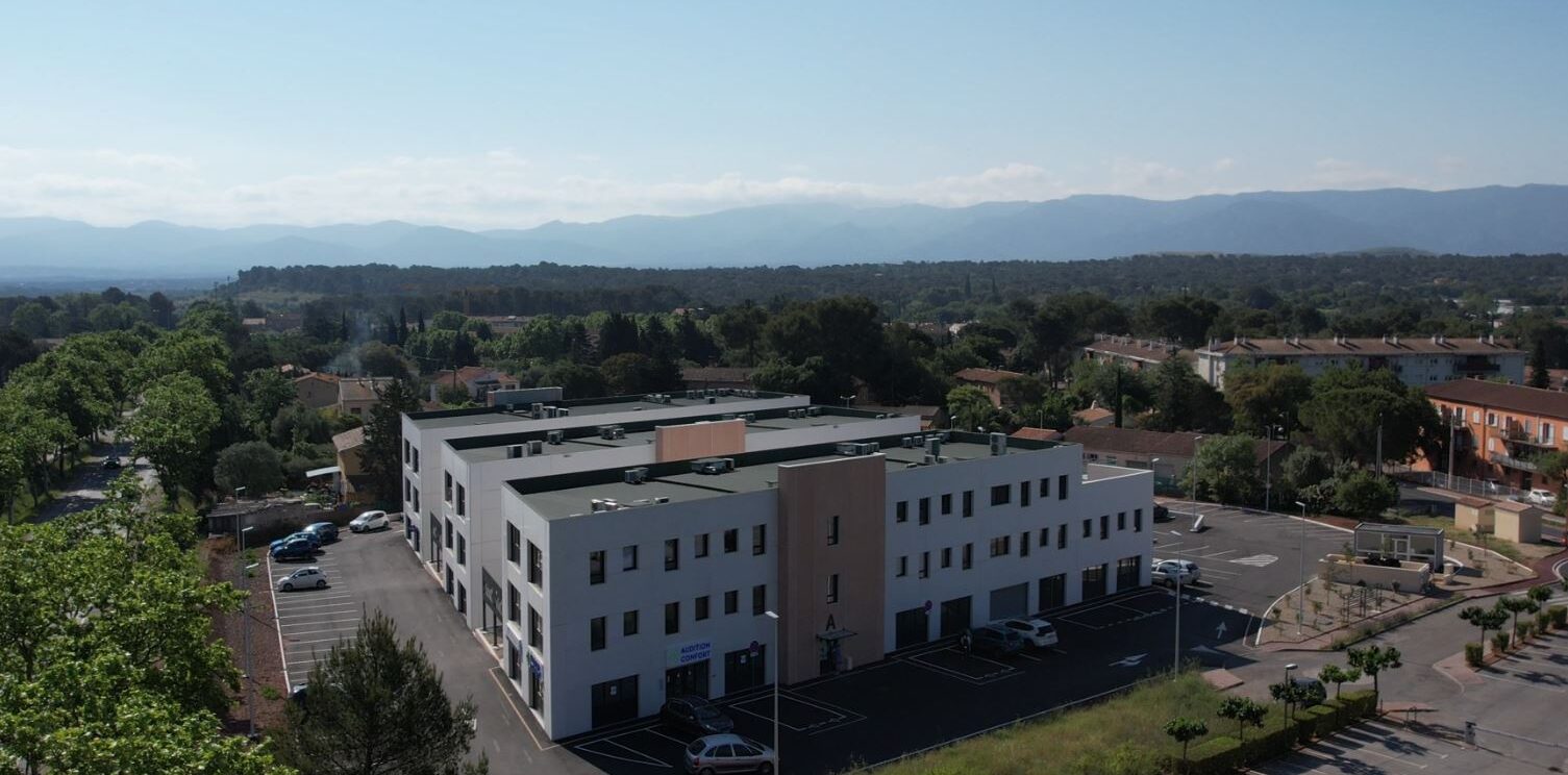 trois bâtiments blancs regroupés en un seul entourés d'un parking et de verdure